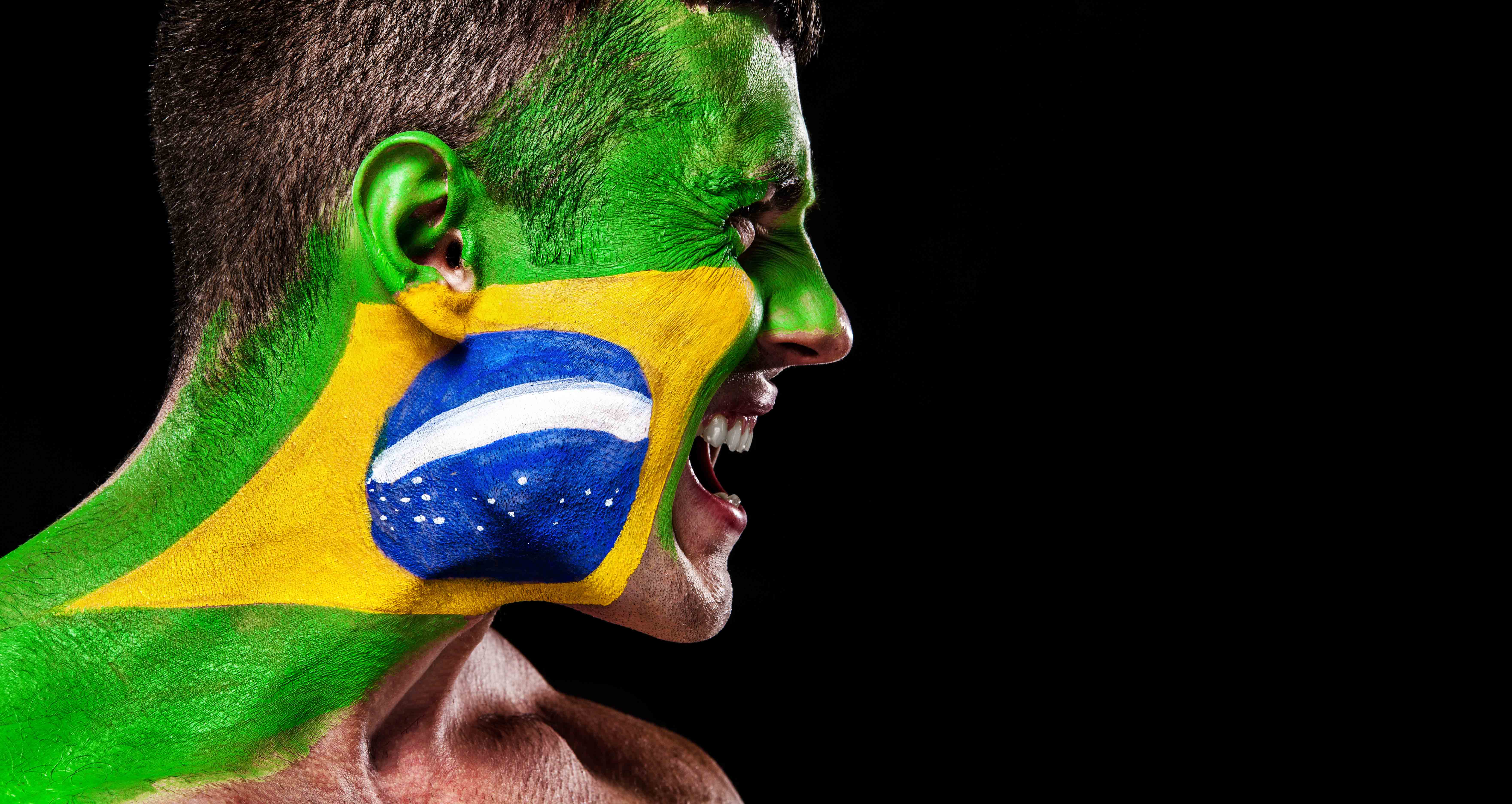 Soccer or football fan with bodyart on face with agression – flag of Brazil.